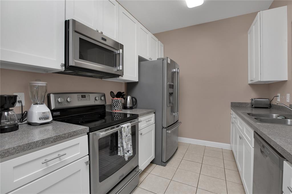 A kitchen features white cabinets, stainless steel appliances, gray countertops, and light-colored tile flooring — 3190 DANTE DRIVE UNIT 304, ORLANDO, FL