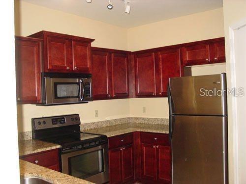 A kitchen features cherry wood cabinets, granite countertops, and stainless steel appliances — 1321 ARBOR VISTA LOOP UNIT 209, LAKE MARY, FL