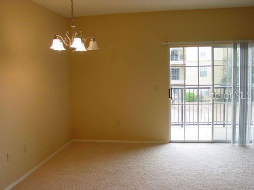 An empty room with beige carpet, tan walls, a chandelier, and sliding glass balcony doors — 1321 ARBOR VISTA LOOP UNIT 209, LAKE MARY, FL