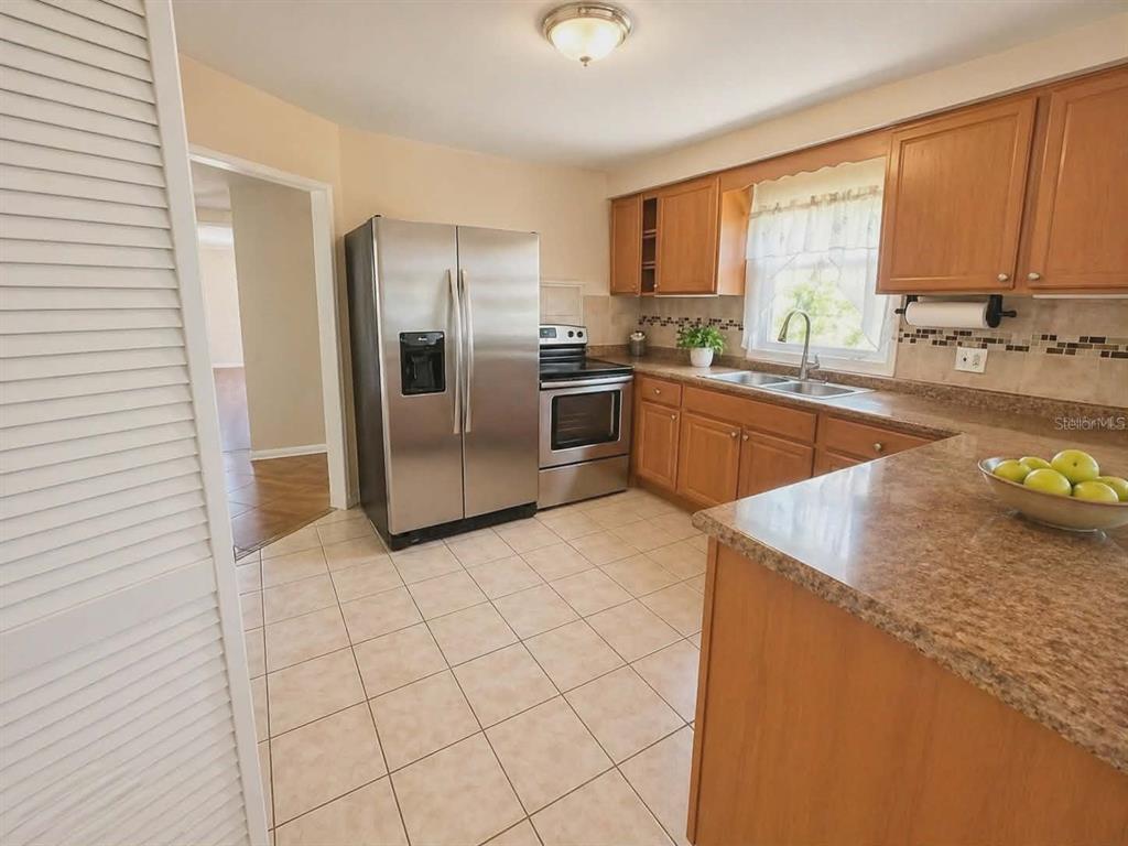 A kitchen features wood cabinets, granite countertops, stainless steel appliances, and light tile flooring — 5230 11TH AVENUE S, GULFPORT, FL