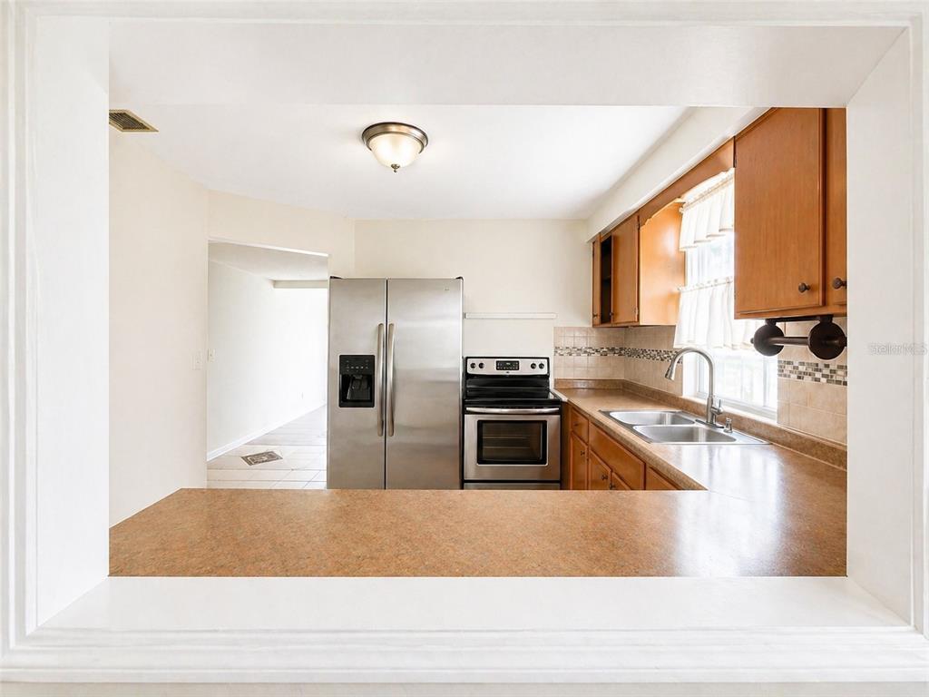 A kitchen with stainless steel appliances, wood cabinets, and a pass-through counter opening — 5230 11TH AVENUE S, GULFPORT, FL