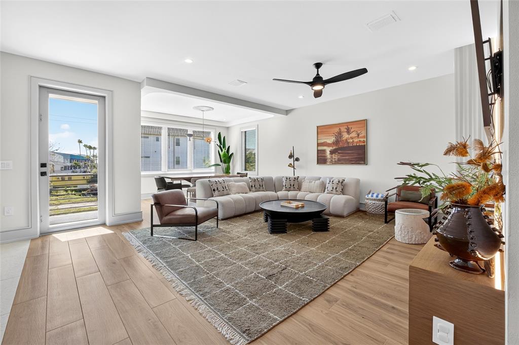 A modern living room features a sectional sofa, area rug, and dining area with windows — 100 12TH STREET N, BRADENTON BEACH, FL