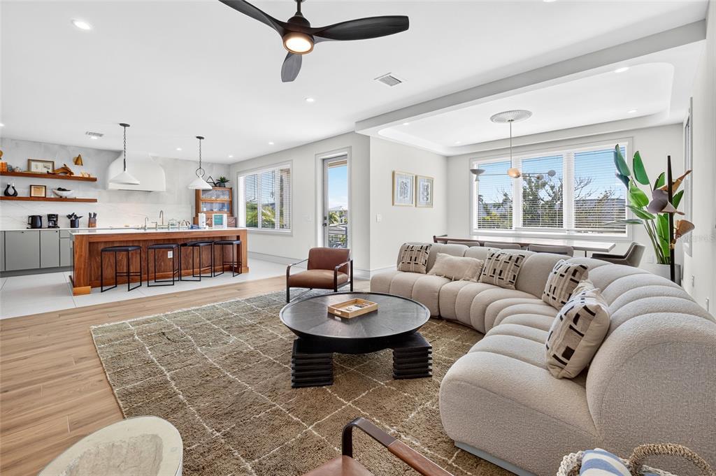 This open-concept living room and kitchen features a curved sofa, wood flooring, and island seating — 100 12TH STREET N, BRADENTON BEACH, FL