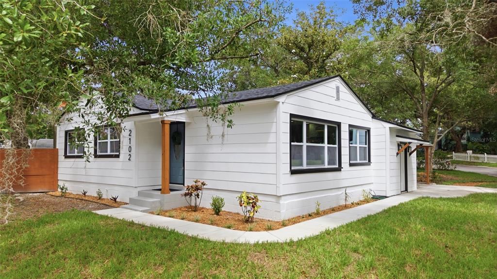 A white single-story house with black window frames and a wooden porch support post — 2102 E HOWELL STREET, TAMPA, FL