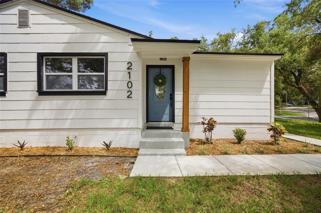 A white house exterior features a blue front door, black window trim, and a wooden post — 2102 E HOWELL STREET, TAMPA, FL