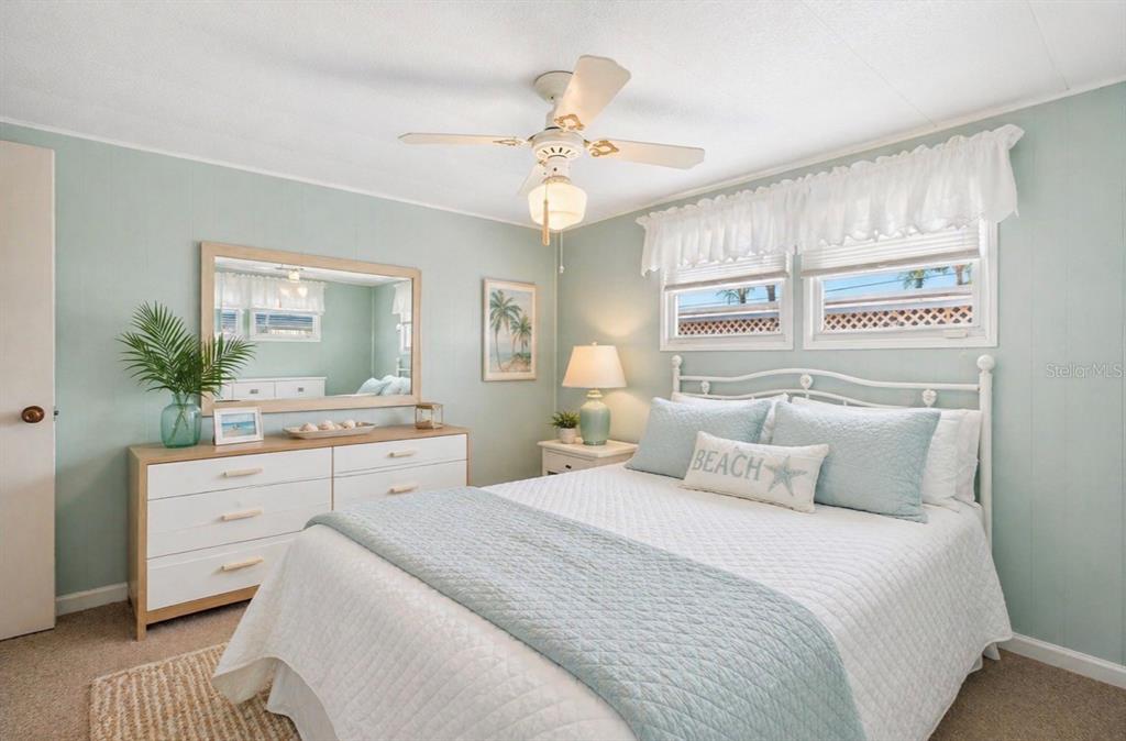 A bedroom features light blue walls, a white bed, a dresser with a mirror, and a ceiling fan — 2000 E BAY DRIVE UNIT 85, LARGO, FL
