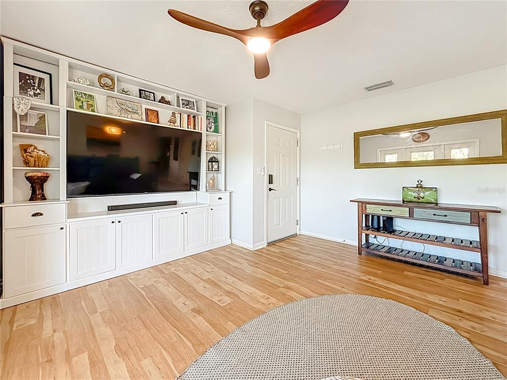 A living room features a built-in media center, wood flooring, and a ceiling fan — 3893 POMPANO DRIVE SE UNIT C, ST PETERSBURG, FL