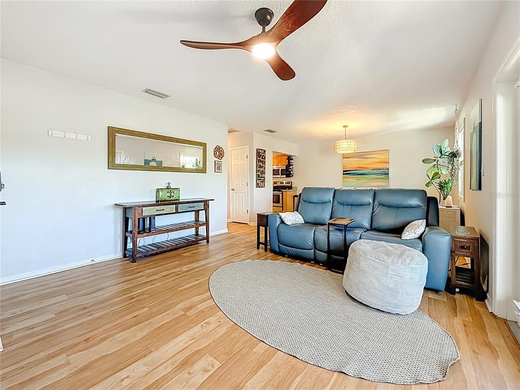 A living room features light wood flooring, a blue leather sofa, and a ceiling fan — 3893 POMPANO DRIVE SE UNIT C, ST PETERSBURG, FL