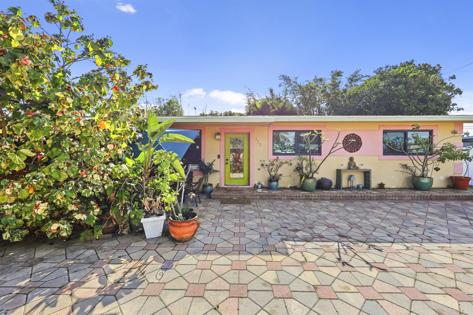 A single-story house with a lime green door, pink trim, and a paved front courtyard — 112 San Juan Drive, Palm Springs FL 33461, PALM SPRINGS, FL
