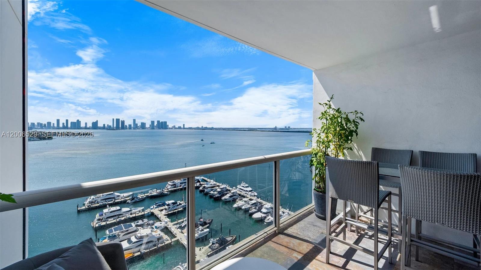 A balcony with outdoor seating overlooks a marina and a distant city skyline — 1900 Sunset Harbour Dr # 2008, Miami Beach FL 33139, MIAMI BEACH, FL