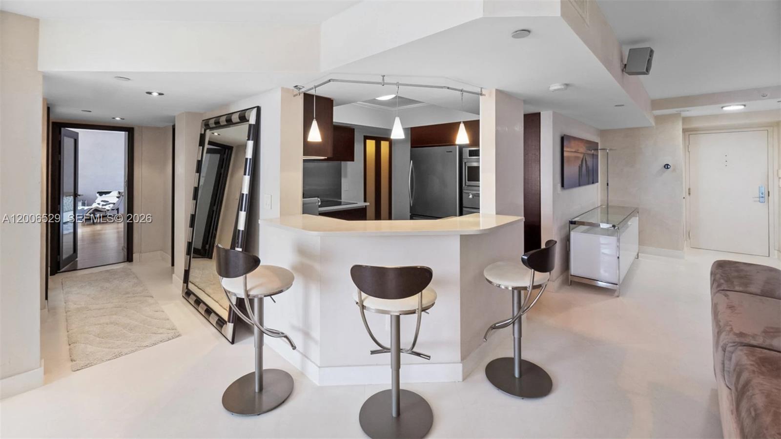 A kitchen with a breakfast bar and three stools sits in an open-concept living space — 1900 Sunset Harbour Dr # 2008, Miami Beach FL 33139, MIAMI BEACH, FL
