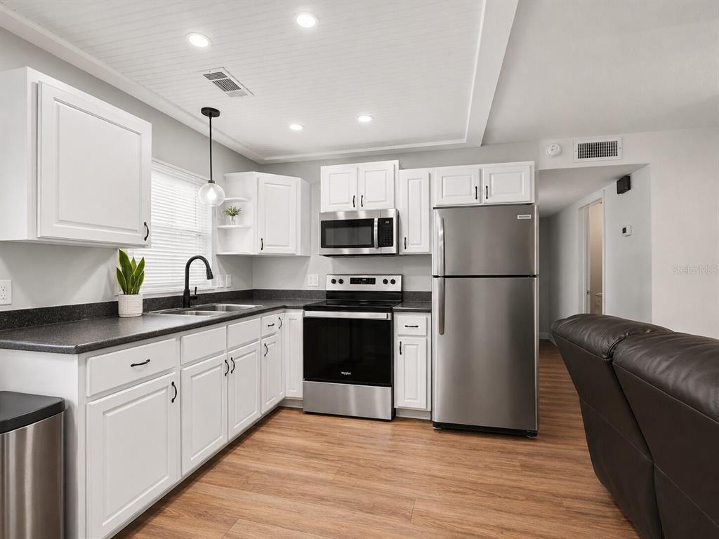 A kitchen features white cabinets, stainless steel appliances, dark countertops, and light wood-look flooring — 2508 AVENUE A SW, WINTER HAVEN, FL