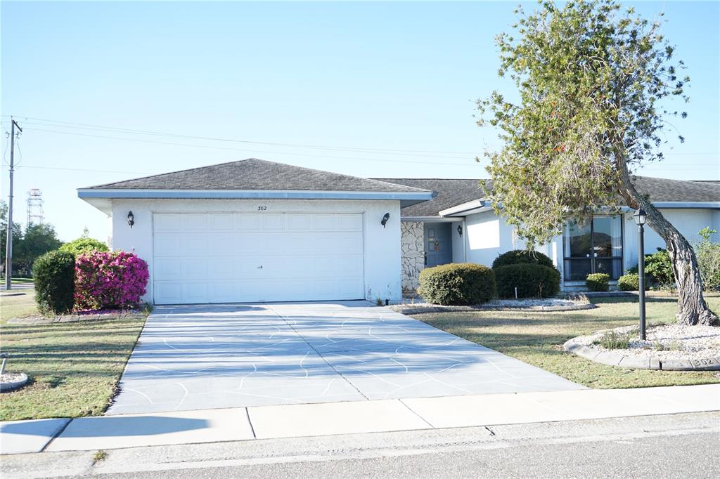A single-story house with a white garage, a patterned driveway, and a large tree — 302 BRYCE COURT, SUN CITY CENTER, FL