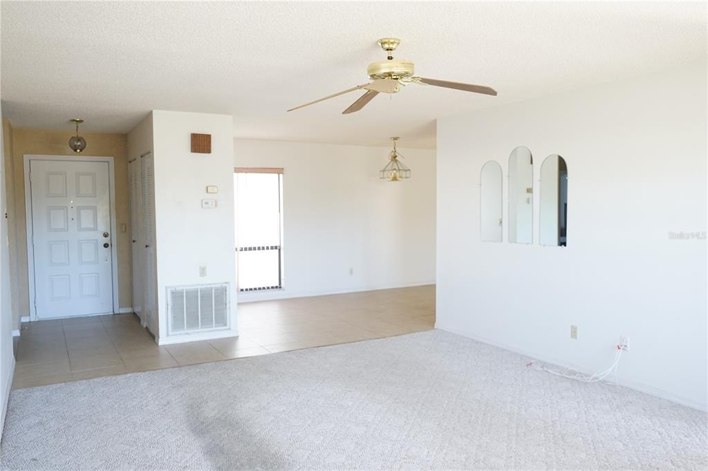 An open-concept living area features a carpeted floor, tiled entryway, ceiling fan, and arched mirrors — 302 BRYCE COURT, SUN CITY CENTER, FL
