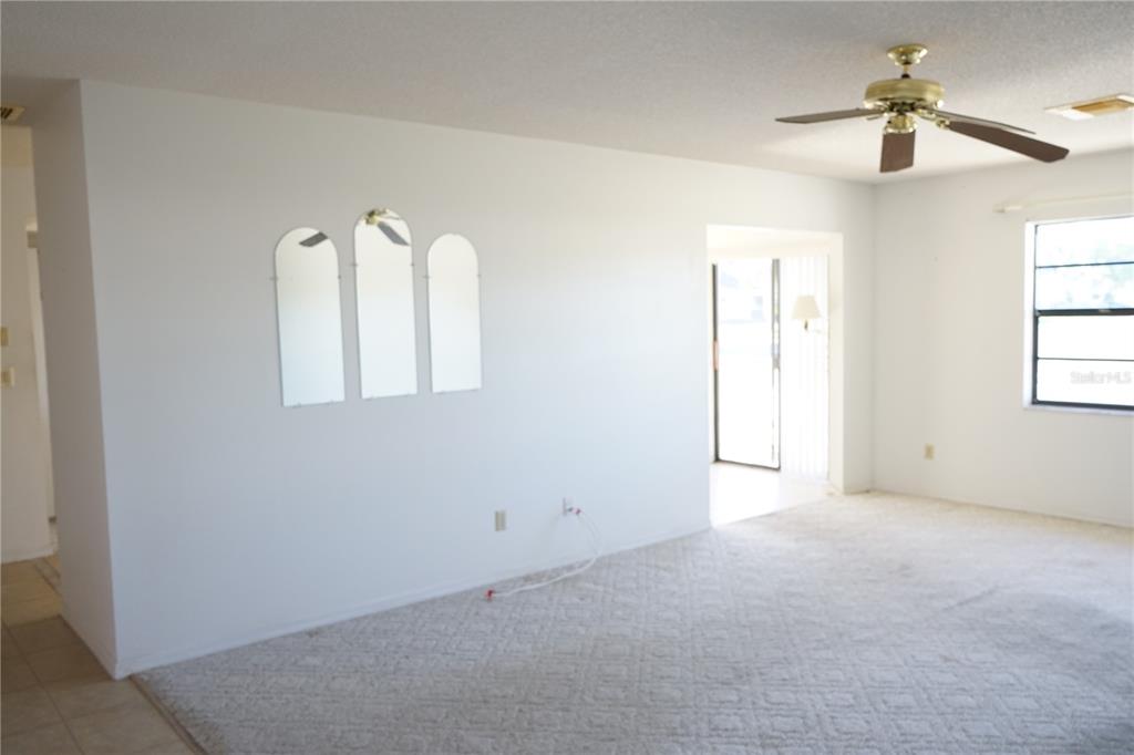 A living room features white walls, beige carpeting, a ceiling fan, and three arched mirrors — 302 BRYCE COURT, SUN CITY CENTER, FL