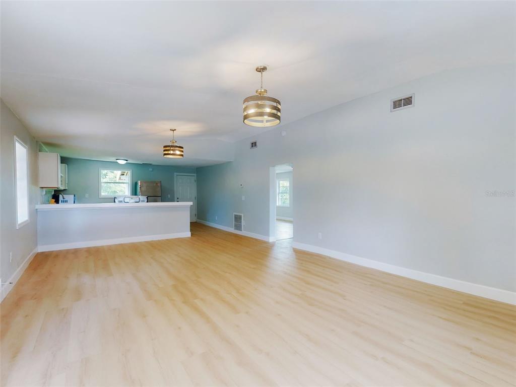 A spacious living room with light wood-look flooring, two pendant lights, and an open kitchen — 1103 WASHINGTON STREET, NEW SMYRNA BEACH, FL