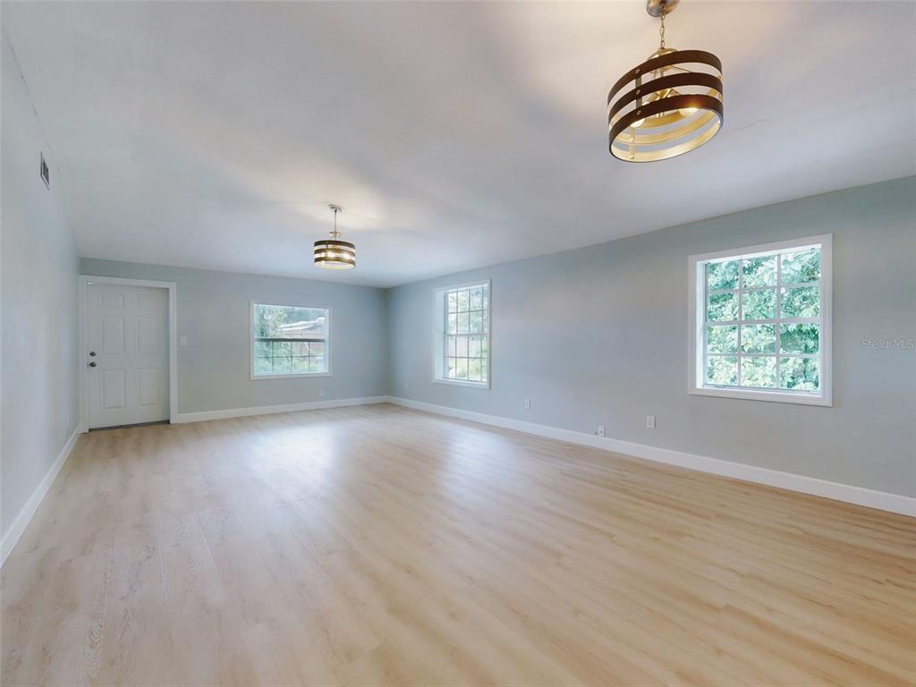 An empty room with light wood-look flooring, pale blue walls, and two modern drum chandeliers — 1103 WASHINGTON STREET, NEW SMYRNA BEACH, FL