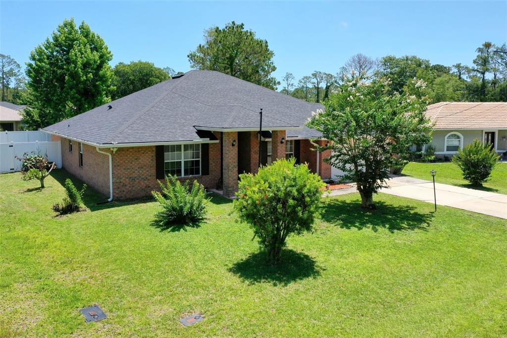 A brick house with a dark shingled roof sits on a grassy lot with trees — 25 PILLORY LANE, PALM COAST, FL