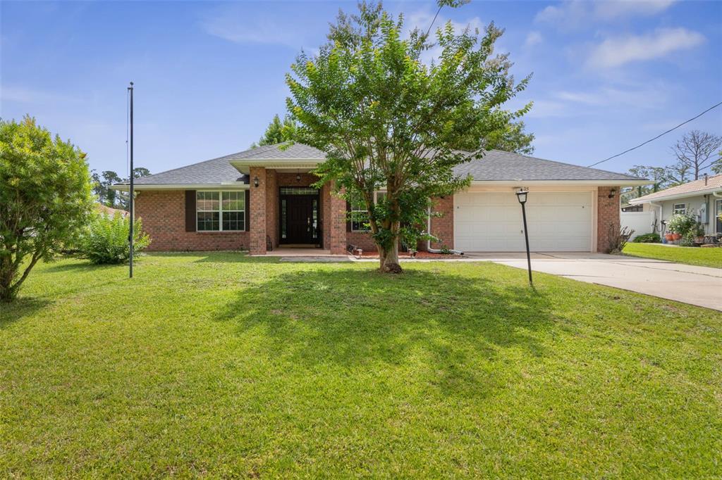 A single-story brick house with a two-car garage and a large tree in the yard — 25 PILLORY LANE, PALM COAST, FL