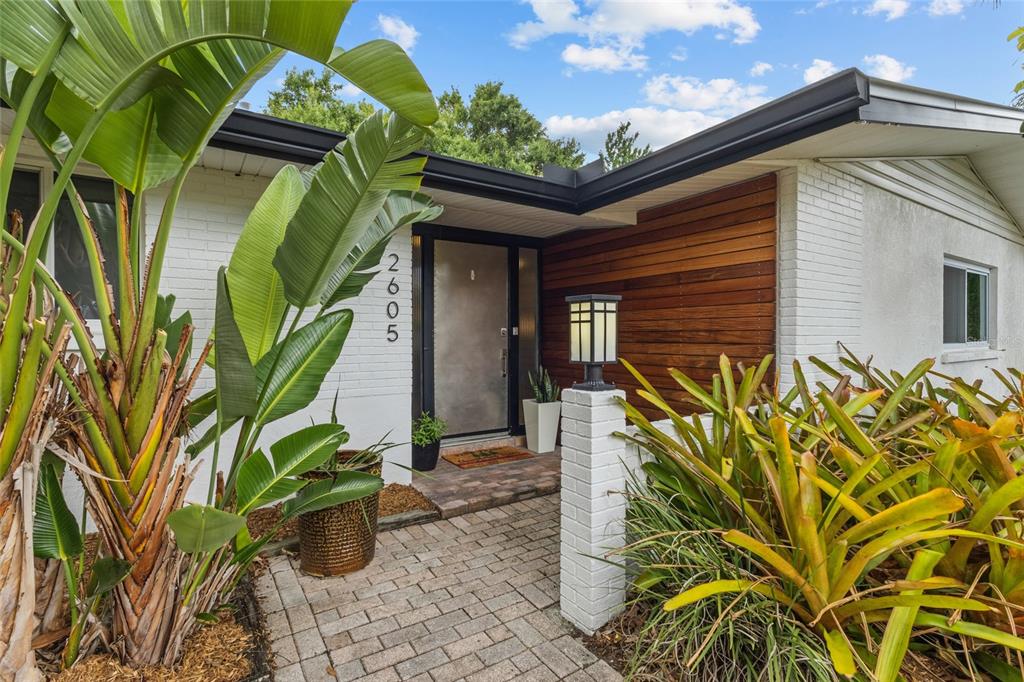 A paved walkway leads to the front entrance of a house with white brick walls — 2605 BOTANY AVENUE, SARASOTA, FL