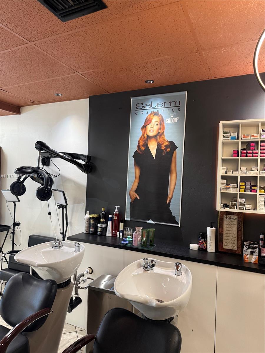 A hair salon features two shampoo sinks, a wall-mounted advertisement, and shelves of hair products — 7764 NW 44, Sunrise FL 33351, SUNRISE, FL