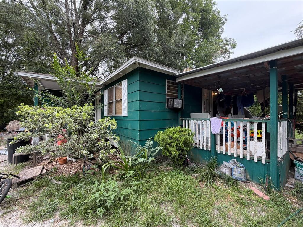 A green, single-story house features a covered porch with a white railing and overgrown landscaping — 39412 MERCER ROAD, DADE CITY, FL