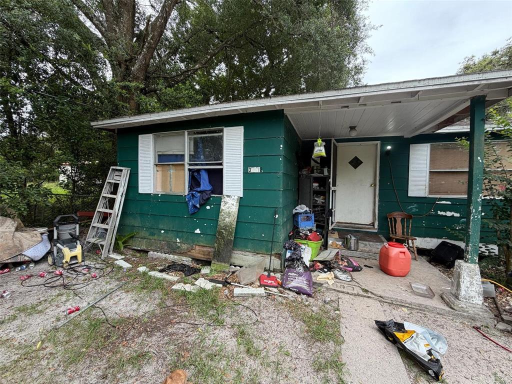A green, single-story house exterior with a cluttered porch, a ladder, and debris in the yard — 39412 MERCER ROAD, DADE CITY, FL