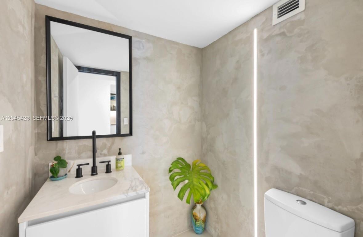 A modern bathroom features a white vanity, a black-framed mirror, and textured concrete-style walls — 2655 Collins Ave # 504, Miami Beach FL 33140, MIAMI BEACH, FL