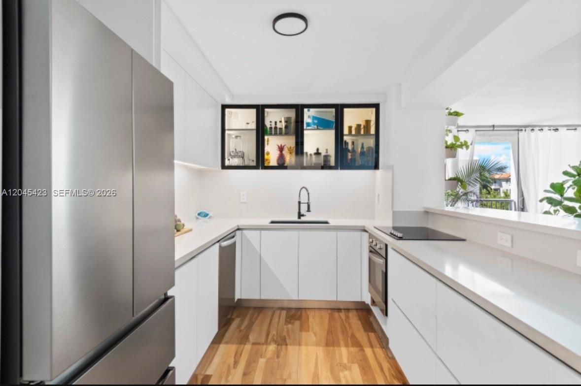 A modern kitchen features white flat-panel cabinets, stainless steel appliances, and wood flooring — 2655 Collins Ave # 504, Miami Beach FL 33140, MIAMI BEACH, FL