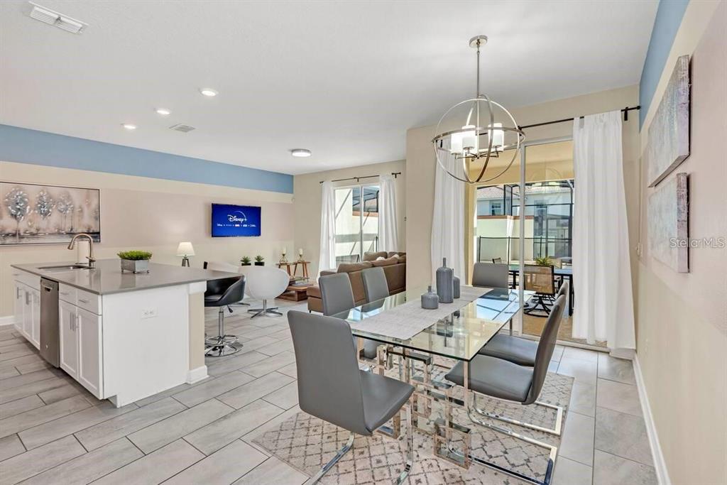 An open-concept kitchen and dining area features a glass table, gray chairs, and island seating — 1565 PLUNKER DRIVE, DAVENPORT, FL
