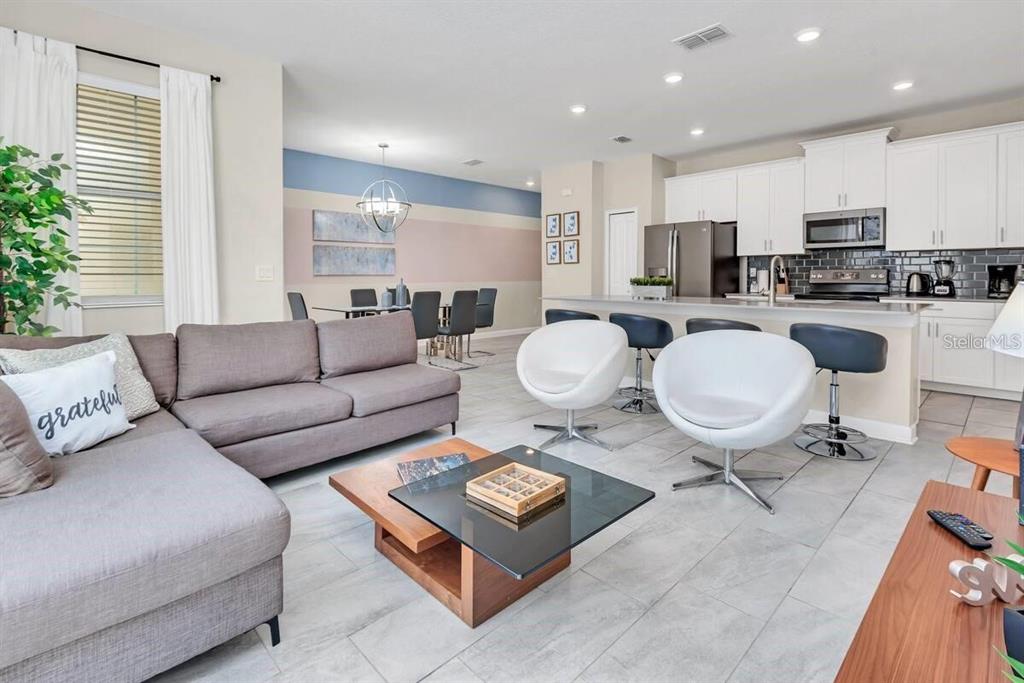 An open-concept living room and kitchen featuring a grey sectional, white swivel chairs, and tile flooring — 1565 PLUNKER DRIVE, DAVENPORT, FL