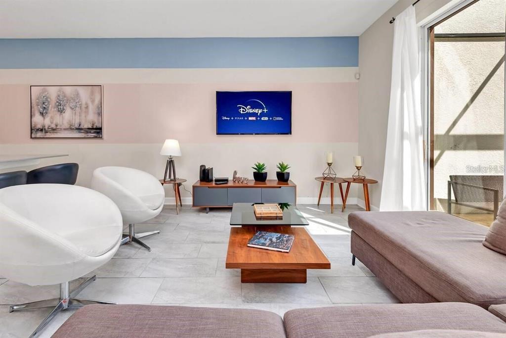 A living room features a color-blocked wall, a mounted television, white swivel chairs, and tile flooring — 1565 PLUNKER DRIVE, DAVENPORT, FL