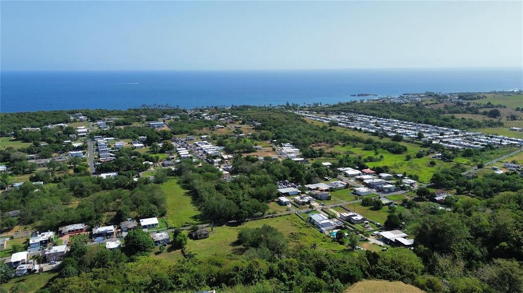 An aerial view shows a coastal neighborhood with houses, green vegetation, and the ocean — SOLAR 4 BO YEGUADA, CAMUY, PR