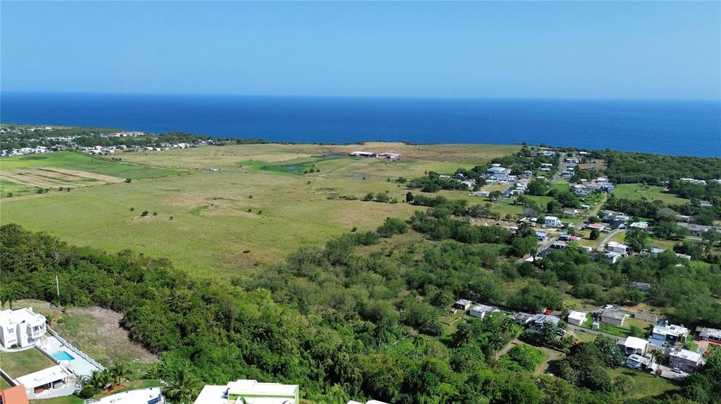An aerial view shows a coastal landscape with green fields, scattered houses, and the ocean — SOLAR 4 BO YEGUADA, CAMUY, PR