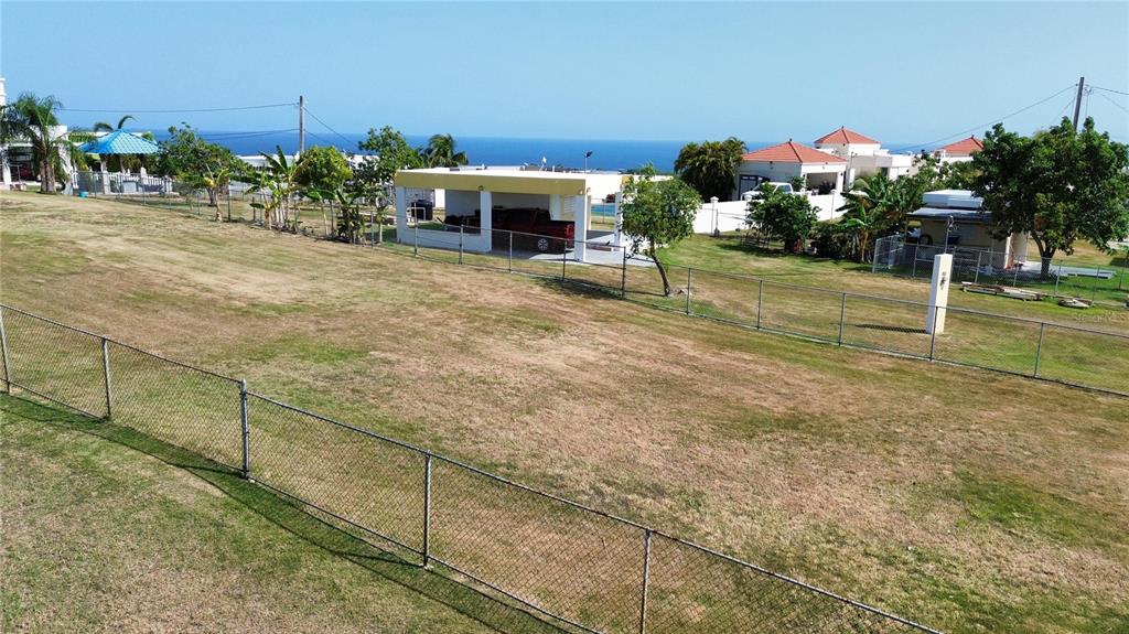 An aerial view shows a fenced, grassy lot with a carport and distant ocean view — SOLAR 4 BO YEGUADA, CAMUY, PR