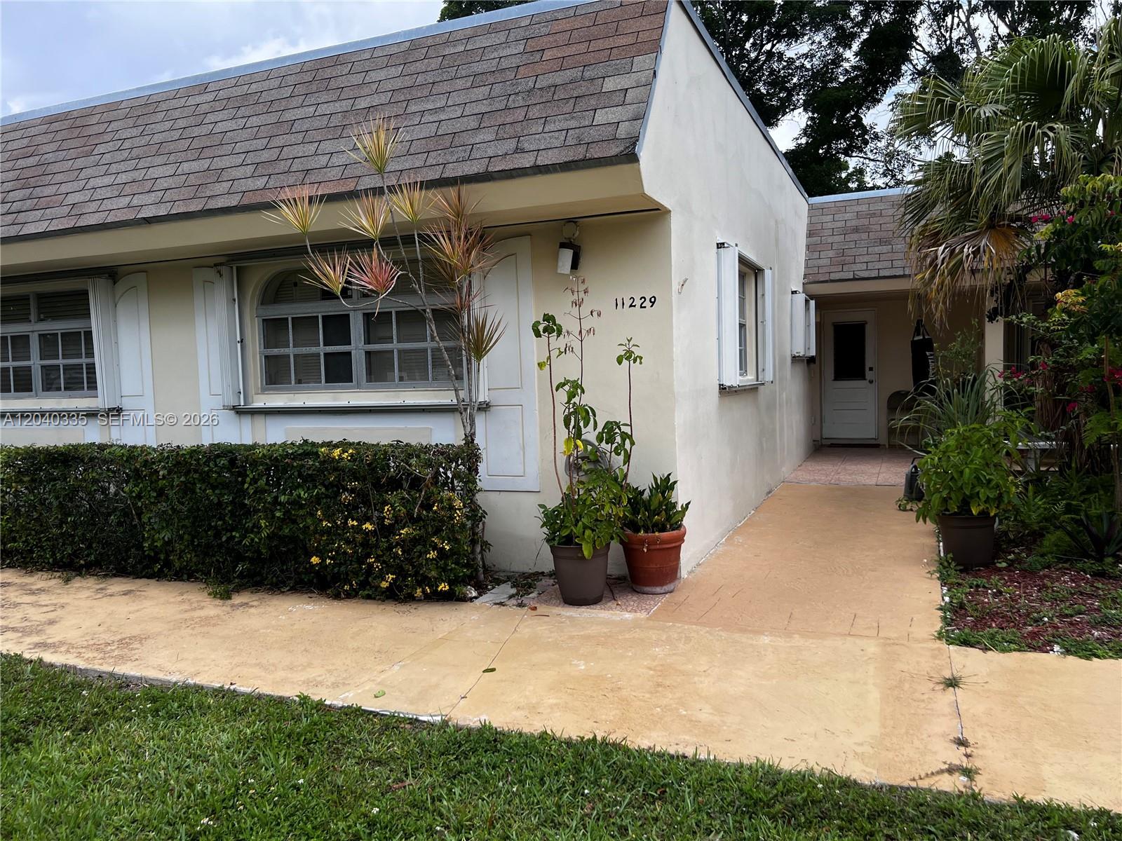 A single-story building exterior features a tan stucco facade, shingled roof, and a walkway — 11229 SW 169th St # V4742, Miami FL 33157, MIAMI, FL