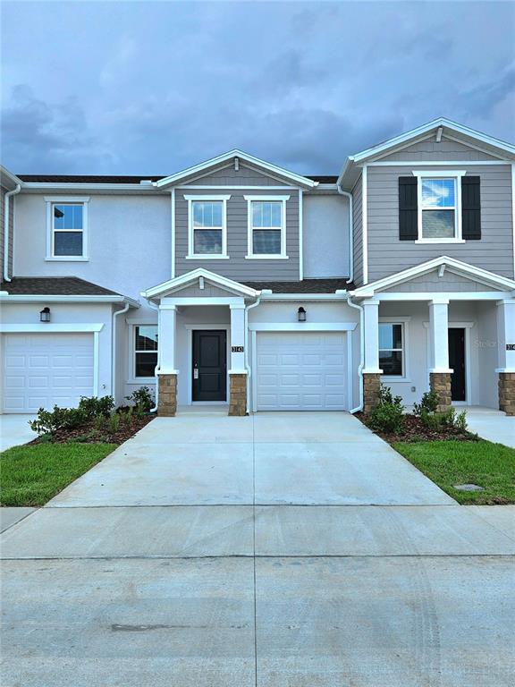 The exterior of a two-story townhouse features a light-colored facade, two garages, and gray siding — 3143 MINDFULLNESS DRIVE, CLERMONT, FL