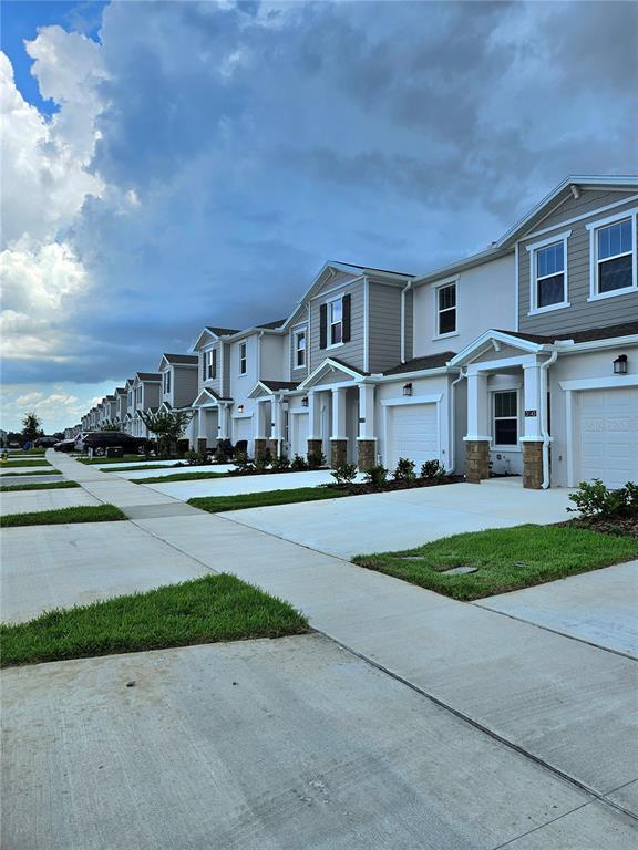 A row of modern two-story townhouses with attached garages and concrete driveways under a cloudy sky — 3143 MINDFULLNESS DRIVE, CLERMONT, FL