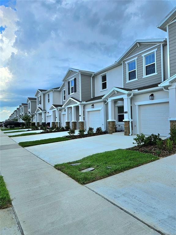 A row of modern two-story townhouses features light-colored siding, attached garages, and concrete driveways — 3143 MINDFULLNESS DRIVE, CLERMONT, FL