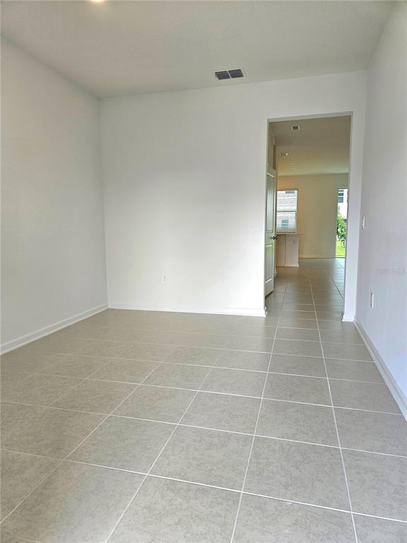 A room with light-colored tile flooring and white walls leads into an adjacent living area — 3143 MINDFULLNESS DRIVE, CLERMONT, FL