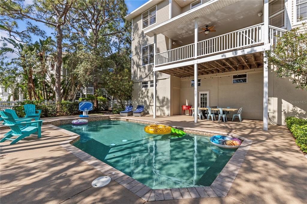 A swimming pool with floats sits on a patio beside a two-story house with balconies — 897 POINT SEASIDE DRIVE, CRYSTAL BEACH, FL