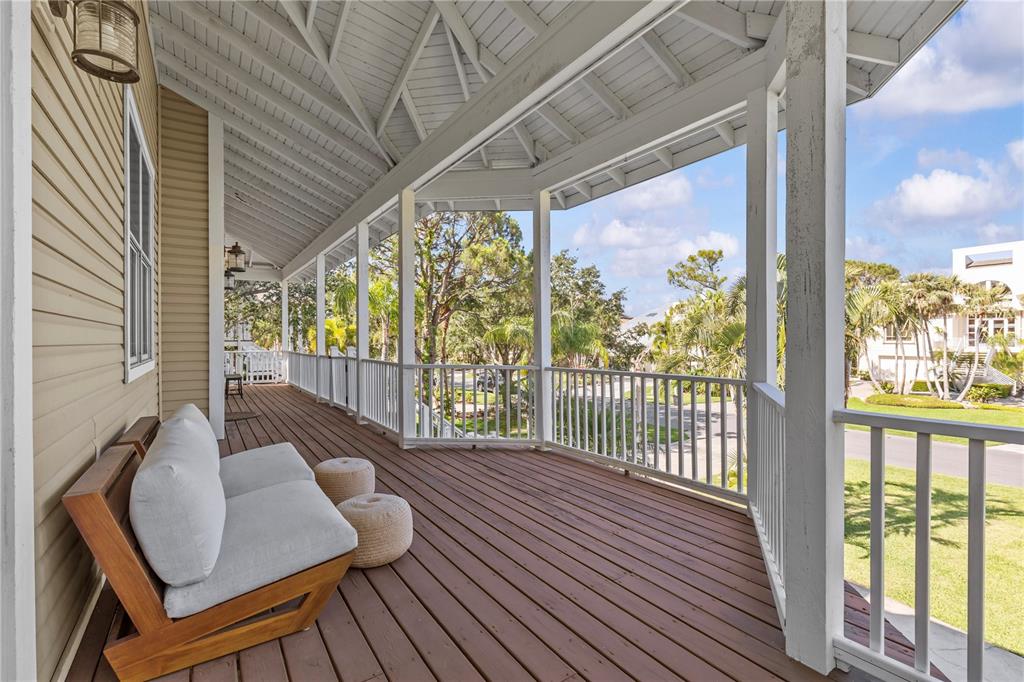 A covered wooden deck features a modern sofa, two poufs, and white railings overlooking trees — 897 POINT SEASIDE DRIVE, CRYSTAL BEACH, FL
