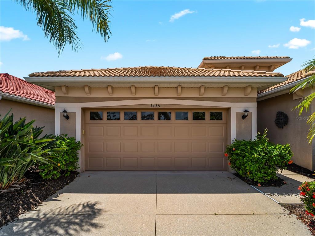 A tan two-car garage with a tiled roof and decorative corbels under the eaves — 5435 BLUE HERON CIRCLE, NORTH PORT, FL