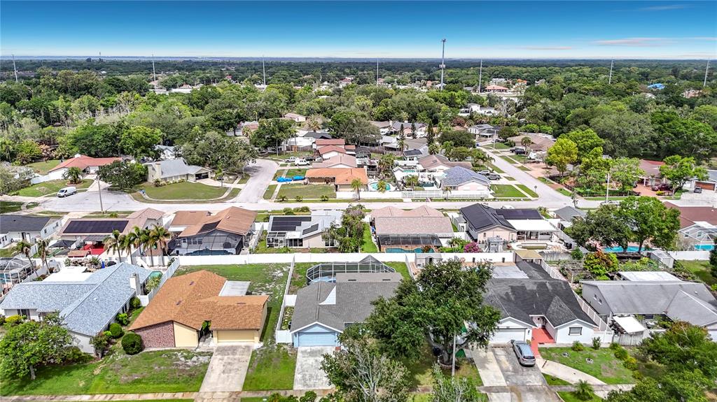 An aerial view shows a suburban neighborhood with single-family homes, driveways, and surrounding green trees — 7010 COBBLEWOOD COURT, TAMPA, FL