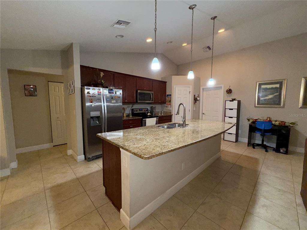A kitchen features a granite-topped island, dark wood cabinetry, and stainless steel appliances — 9670 SW 42ND AVENUE, OCALA, FL
