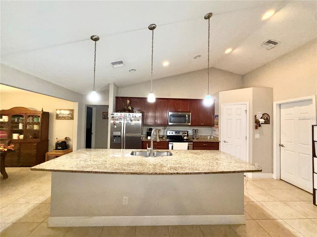 A kitchen features a large granite-topped island, dark wood cabinetry, and three pendant lights — 9670 SW 42ND AVENUE, OCALA, FL