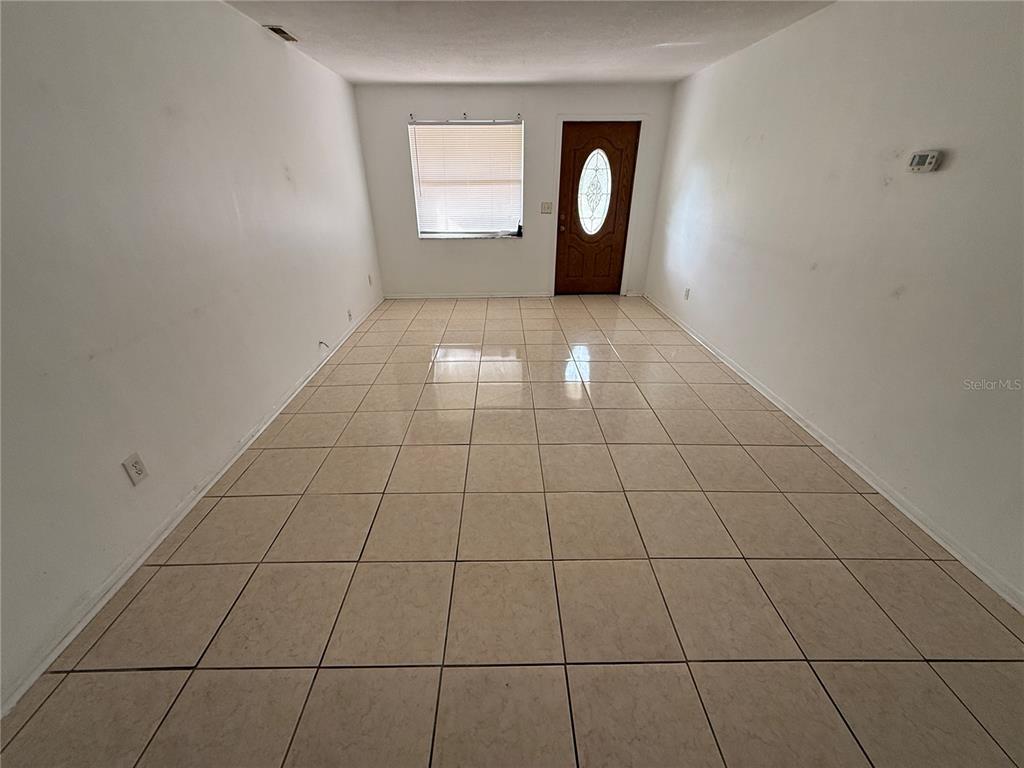 An empty room features white walls, a brown front door, and light-colored square floor tiles — 1270 8TH AVENUE NE, LARGO, FL