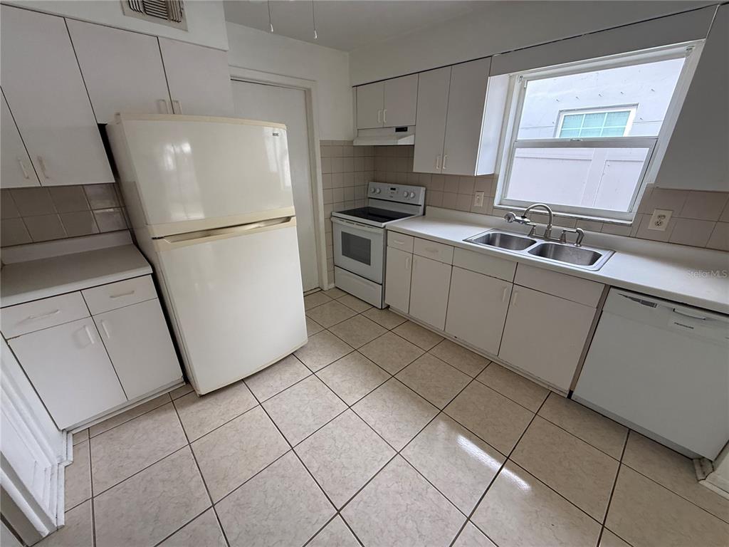 A kitchen features white cabinets, white appliances, a double sink, and light-colored tile flooring — 1270 8TH AVENUE NE, LARGO, FL