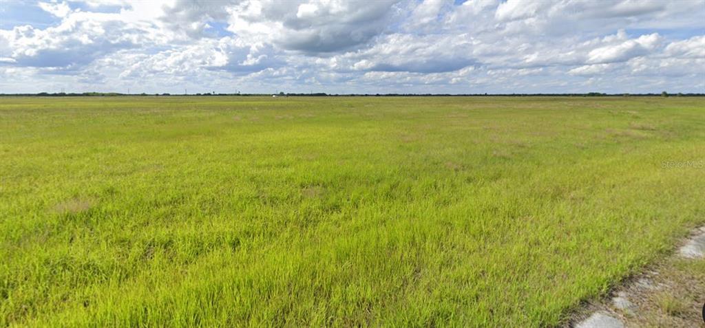 A wide, flat, grassy field stretches toward a distant horizon under a cloudy blue sky — 2468 OCONEE AVENUE SW, PALM BAY, FL