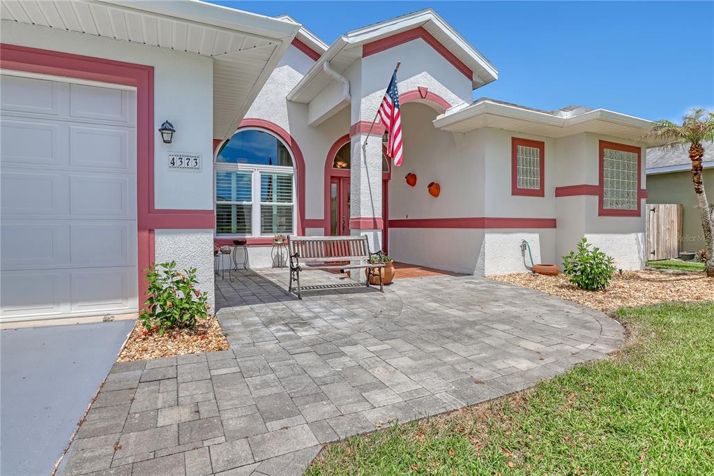 A paved patio leads to the front entrance of a house with white stucco walls — 4373 FLETCHER LANE, TITUSVILLE, FL